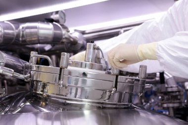 İlaç üretimi için büyük bir rektör. Adam reaktör kapak kapatır. Süspansiyon ekstresinin hazırlanması. İlaç fabrikası reaktör. Tıbbi sanayi.