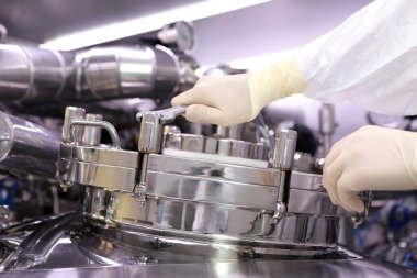 İlaç üretimi için büyük bir rektör. Adam reaktör kapak kapatır. Süspansiyon ekstresinin hazırlanması. İlaç fabrikası reaktör. Tıbbi sanayi.