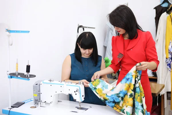 Beautiful girl in a red dress in a tailoring studio. Exclusive tailoring of dresses to order. The girl sews a dress on a sewing machine. European woman works in a sewing workshop.