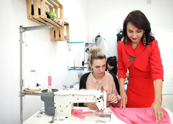 Belle fille en robe rouge dans un atelier de couture. Couture exclusive de robes sur commande. La fille coud une robe sur une machine à coudre. Femme européenne travaille dans un atelier de couture . — Photo