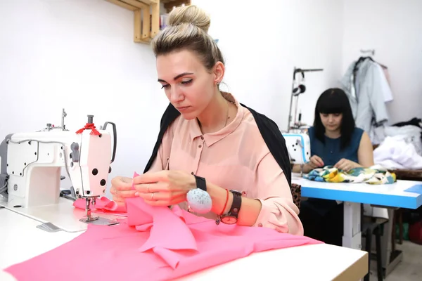 Beautiful girl in a red dress in a tailoring studio. Exclusive tailoring of dresses to order. The girl sews a dress on a sewing machine. European woman works in a sewing workshop.