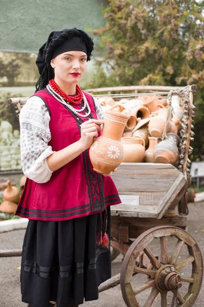 民族衣装の美しい女の子。彼の手に古代の鍋を保持します。19世紀後半のアンティークの服。女性の美しいドレスやスカート。農村生活、国家の伝統の概念 — ストック写真