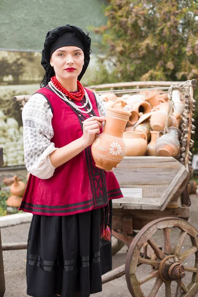 穿着民族服装的漂亮姑娘。手里拿着一个古老的壶。19世纪末的古董服装。女人穿上漂亮的衣服和裙子.农村生活的概念、民族传统 — 图库照片