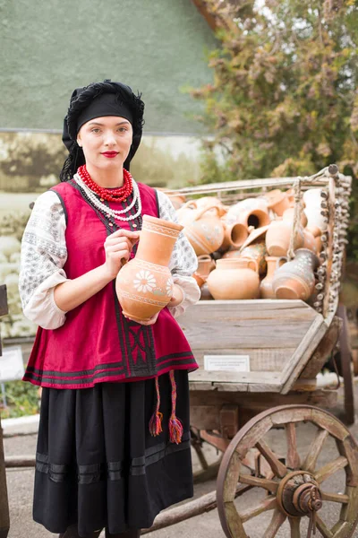 Menina bonita em vestido nacional. Segurando um pote antigo em suas mãos. Roupas antigas do final do século XIX. Belo vestido e saia em uma mulher. O conceito de vida rural, tradições nacionais — Fotografia de Stock