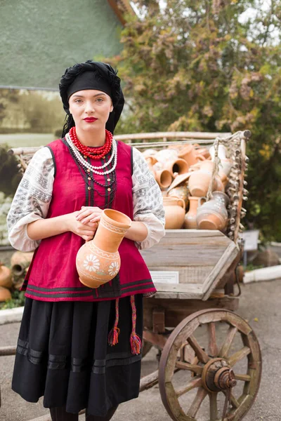 穿着民族服装的漂亮姑娘。手里拿着一个古老的壶。19世纪末的古董服装。女人穿上漂亮的衣服和裙子.农村生活的概念、民族传统 — 图库照片
