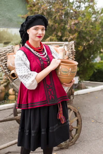 Hermosa chica en vestido nacional. Llevando una olla antigua en sus manos. Ropa antigua de finales del siglo XIX. Hermoso vestido y falda en una mujer. El concepto de vida rural, tradiciones nacionales —  Fotos de Stock