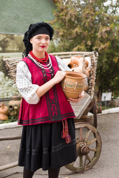 Bella ragazza in abito nazionale. Teneva in mano un'antica pentola. Abbigliamento antico della fine del XIX secolo. Bellissimo vestito e gonna su una donna. Il concetto di vita rurale, tradizioni nazionali — Foto Stock