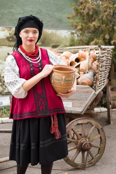 Bella ragazza in abito nazionale. Teneva in mano un'antica pentola. Abbigliamento antico della fine del XIX secolo. Bellissimo vestito e gonna su una donna. Il concetto di vita rurale, tradizioni nazionali — Foto Stock