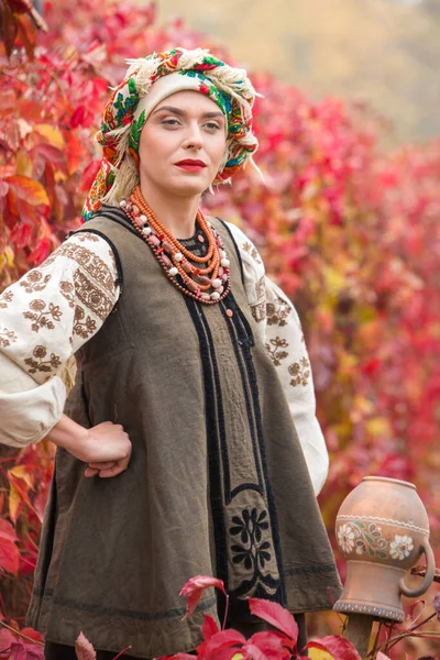 Piękna dziewczyna w sukience narodowej. Starożytnym glinianym garnkiem. Starożytna odzież z końca XIX wieku. Piękna sukienka i spódnica na kobiecie. Piękna jesień i liście. Odzież późnych 19-tych lat — Zdjęcie stockowe