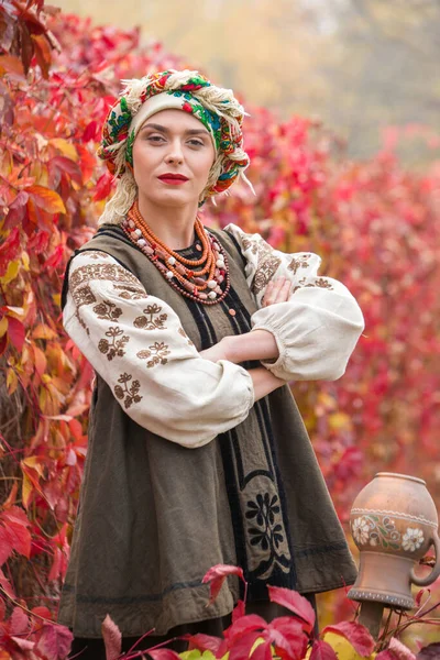 Menina bonita em vestido nacional. Com um pote de barro antigo. Roupas antigas do final do século XIX. Belo vestido e saia em uma mulher. Belo outono e folhas. Vestuário do final do século XIX — Fotografia de Stock