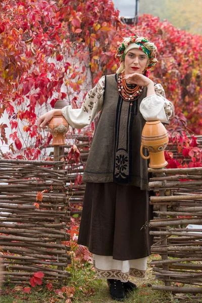 Schöne Mädchen in Nationalkleidung. Mit einem alten Tontopf. Antike Kleidung aus dem späten 19. Jahrhundert. Schönes Kleid und Rock auf eine Frau. Schöner Herbst und Blätter. Kleidung des späten 19. Jahrhunderts — Stockfoto