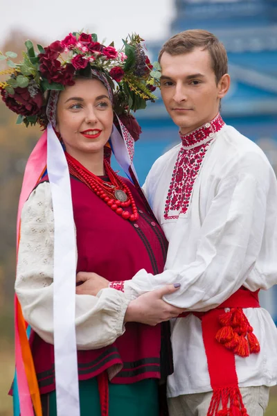 Lány és fickó retro jelmezben az utcán a régi faluban. Egy ősi rítus retro előadása. Gyönyörű koszorú egy lányon. A fickó megöleli a lányt, mindketten mosolyognak. Régi ruhák a késő — Stock Fotó