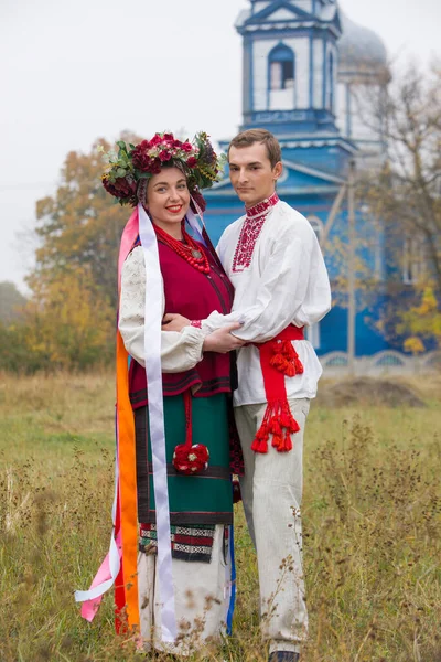 Fille et gars en costumes rétro dans la rue dans le vieux village. Mise en scène rétro d'un rite ancien. Belle couronne sur une fille. Le mec embrasse la fille, les deux sourient. Vêtements anciens de la fin — Photo