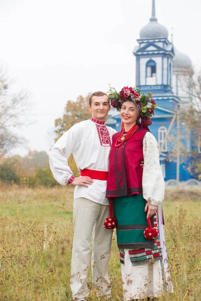 Fille et gars en costumes rétro dans la rue dans le vieux village. Mise en scène rétro d'un rite ancien. Belle couronne sur une fille. Le mec embrasse la fille, les deux sourient. Vêtements anciens de la fin — Photo