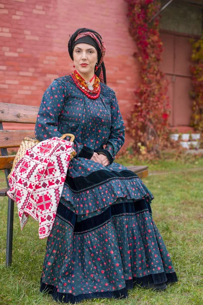 Donna con cesto in abiti retrò del XIX secolo. Abbigliamento antico della fine del XIX secolo. Bellissimo vestito e gonna su una donna. Perline e decorazioni su una ragazza. Un posto antico. Tradizione e — Foto Stock