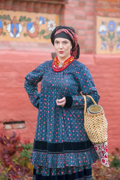 Mulher com uma cesta em roupas retrô do século XIX. Roupas antigas do final do século XIX. Belo vestido e saia em uma mulher. Grânulos e decoração em uma menina. Um lugar antigo. Tradição e — Fotografia de Stock