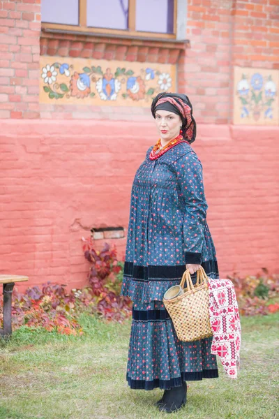 Donna con cesto in abiti retrò del XIX secolo. Abbigliamento antico della fine del XIX secolo. Bellissimo vestito e gonna su una donna. Perline e decorazioni su una ragazza. Un posto antico. Tradizione e — Foto Stock