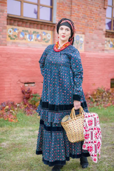 Donna con cesto in abiti retrò del XIX secolo. Abbigliamento antico della fine del XIX secolo. Bellissimo vestito e gonna su una donna. Perline e decorazioni su una ragazza. Un posto antico. Tradizione e — Foto Stock