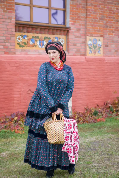 Mulher com uma cesta em roupas retrô do século XIX. Roupas antigas do final do século XIX. Belo vestido e saia em uma mulher. Grânulos e decoração em uma menina. Um lugar antigo. Tradição e — Fotografia de Stock