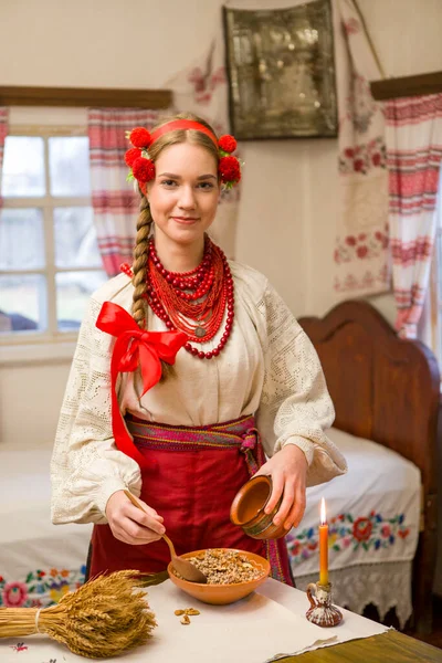 穿着民族服装的漂亮姑娘正在准备喜庆的晚餐.戴着美丽的花环和红色绣花裙。家庭庆祝和民族风俗的庆祝。与kutia -传统的碗 — 图库照片