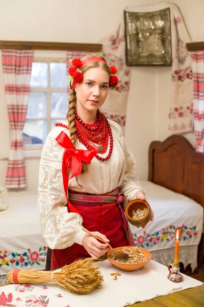 Piękna dziewczyna w sukience narodowej przygotowuje uroczysty obiad. W pięknym wieńcu i czerwonej haftowanej sukience. Rodzinne świętowanie i świętowanie narodowego zwyczaju. Miska z kutią - tradycyjna — Zdjęcie stockowe