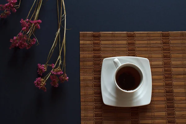 Masaya çiçek koyu mavi zemin üzerine üstten görünüm beyaz fincan çay. Soyut mutfak arka plan.