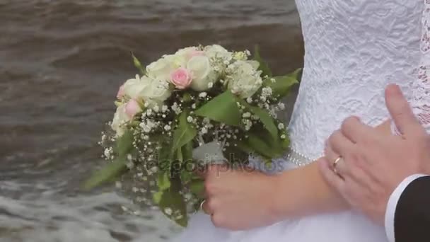 De bruidegom omarmt de bruid strelen van de arm in de buurt van de zee. Trouwdag — Stockvideo