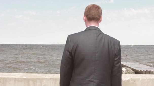 Joven hombre de negocios que viene al muelle y mira al mar — Vídeo de stock