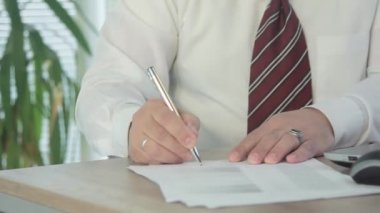 Beyaz gömlekli işadamı önemli bir belgeyi imzalıyor. Çerçeve belgesinde ve elde. Kaydırıcı ile hareket halinde çekim