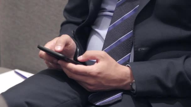 A man sitting on a chair in his jacket is typing something in the phone — Stock Video