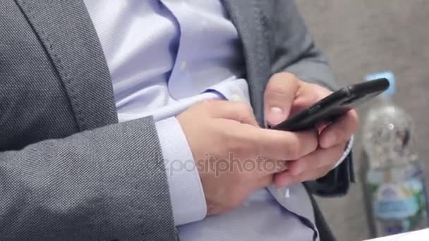 Um homem sentado em uma cadeira de casaco está digitando algo no telefone — Vídeo de Stock