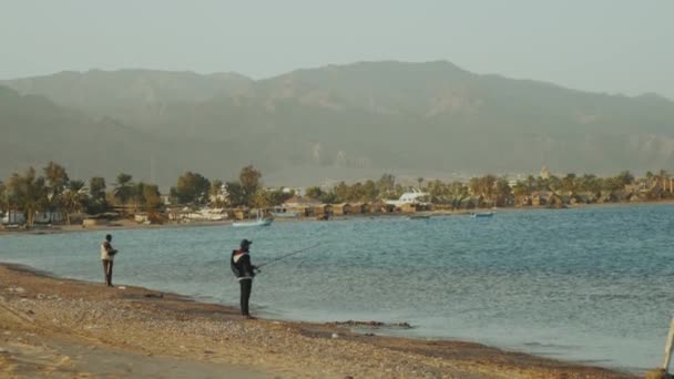 Két halász a tengeren, kis hullámokkal. Férfi halászat fonás a strandról, lassított felvétel. — Stock videók