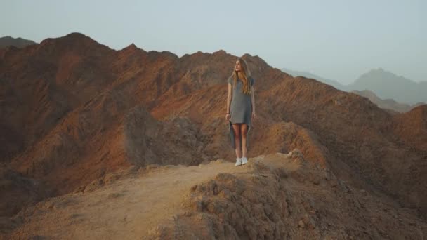 Joven mujer rubia de pie en la cima de la montaña. Paisaje de montaña con puesta de sol, cámara lenta, 4k — Vídeos de Stock