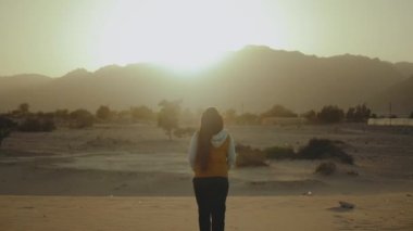 Kız sahilde yürüyüp Horizon 'u araştırıyor. Kadının sırtından kumsal ve mavi deniz manzarası, yavaş çekim, 4k