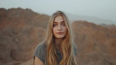 Uzun elbiseli genç sarışın kadın dağın tepesinde yürüyor. Gün batımlı dağ manzarası, yavaş çekim, 4k 