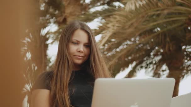 Schöne Studentin oder Freiberuflerin, die an einem Laptop arbeitet, Frau auf Balkon mit Blick auf Palme und Meer, schnelle Videos, Zeitlupe, 4k — Stockvideo