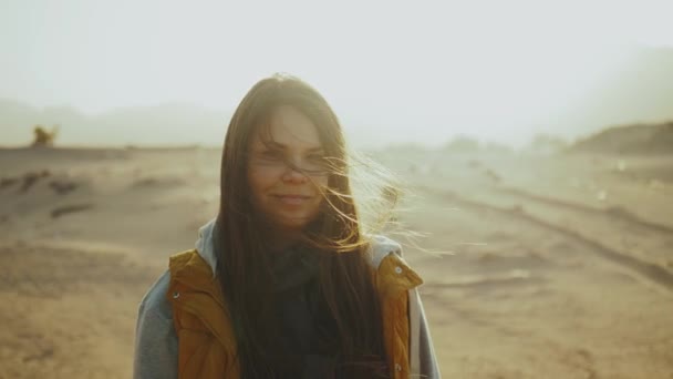 Csinos nő portréja naplementekor. Boldog fiatal nő áll a szélben ellen sivatagi naplemente táj, lassított felvétel. — Stock videók