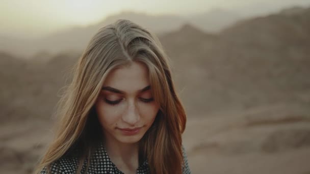 Retrato de una guapa rubia al atardecer. Mujer joven y feliz de pie en una montaña desierta, paisaje de puesta de sol, cámara lenta, 4k — Vídeo de stock