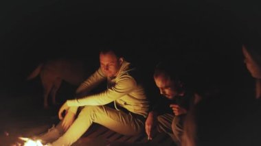 Bir grup arkadaş, gece deniz kenarındaki kumsalda kamp ateşinin yanında eğleniyor. Hızlı video, ağır çekim, 4k