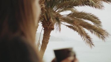 Sabahları balkonda tek başına kahve ya da çay içen bir kadın. Mavi deniz manzaralı, pencereden bakan, hızlı çekim, ağır çekim, 4k