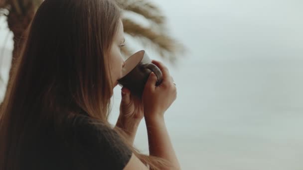 Alleen vrouw is het drinken van koffie of thee in de ochtend op het balkon met blauwe uitzicht op zee, standpunt vanuit het raam, snelle video, slow motion, 4k — Stockvideo