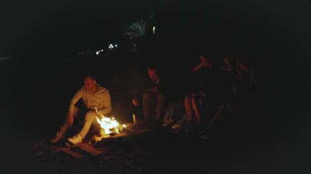 Grupo de amigos se divertindo perto da fogueira na praia perto do mar à noite, vídeo rápido, câmera lenta, 4k — Vídeo de Stock