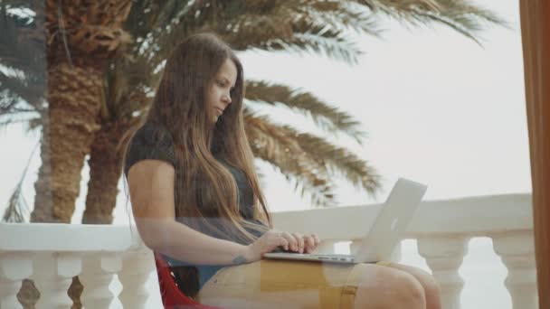 Estudante bonita ou freelancer trabalhando em um laptop, mulher sentada na varanda com vista superior palma e mar, vídeo rápido, câmera lenta, 4k — Vídeo de Stock