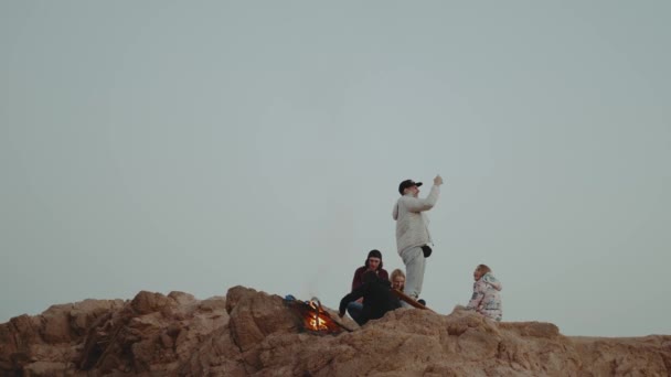 Grupo de amigos relaxando no topo de uma montanha ao pôr-do-sol, sentados perto da fogueira, desfrutando de seu tempo amizade, juventude, câmera lenta, 4k — Vídeo de Stock