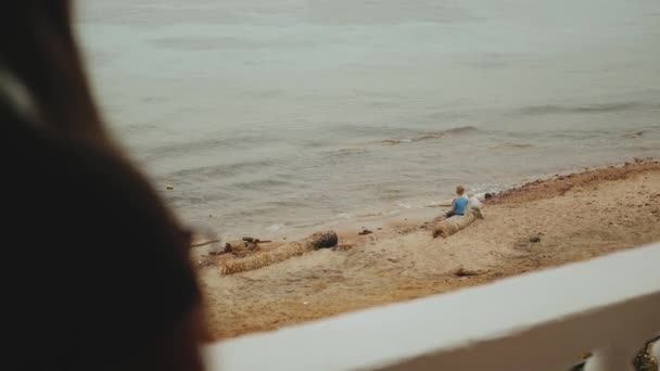 Mujer sola está tomando café o té en la mañana en el balcón con vista al mar azul, los niños juegan en la playa cerca del mar, video rápido, cámara lenta, 4k — Vídeo de stock