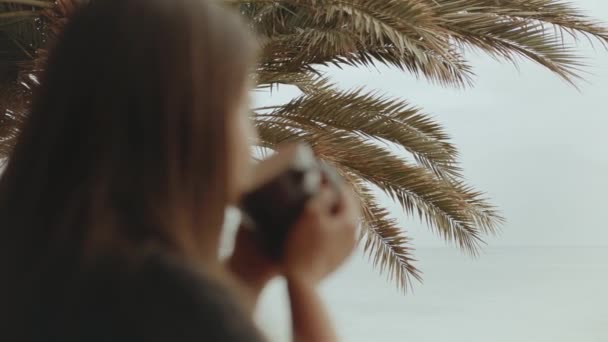 Donna sola sta bevendo caffè o tè al mattino sul balcone con vista mare blu, punto di vista dalla finestra, video rapido, rallentatore, 4k — Video Stock