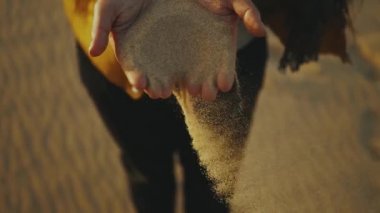 Gün batımında çölde yavaşça parmaklarının arasından kum döken kadına yaklaş, ağır çekimde..