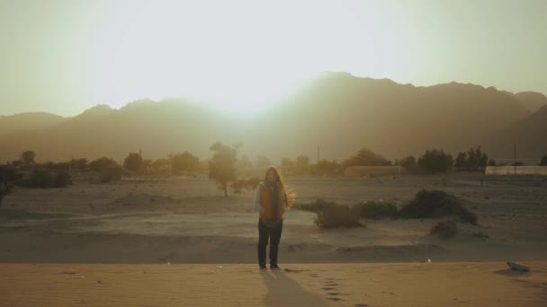 Portrét krásné ženy při západu slunce. Šťastná mladá žena stojící ve větru proti pouštní krajině západu slunce, zpomalený pohyb. — Stock video