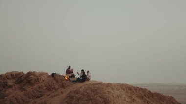 Bir grup arkadaş gün batımında dağın tepesinde, şenlik ateşinin yanında oturup eğleniyorlar - arkadaşlık, gençlik, ağır çekim, 4k 