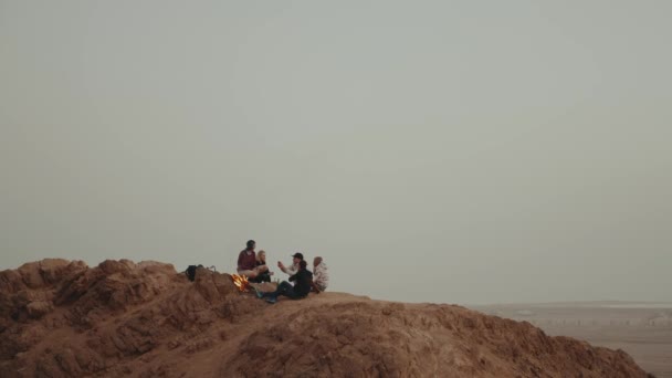 Grupo de amigos relajándose en la cima de una montaña al atardecer, sentados cerca de la hoguera, disfrutando de su tiempo - amistad, juventud, cámara lenta, 4k — Vídeo de stock